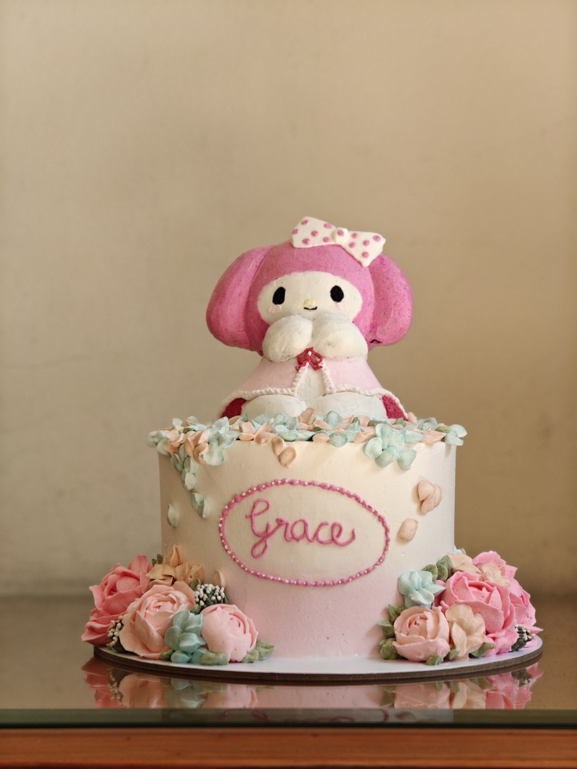 Two-tier cake with kawaii plush doll and cascading fondant flowers